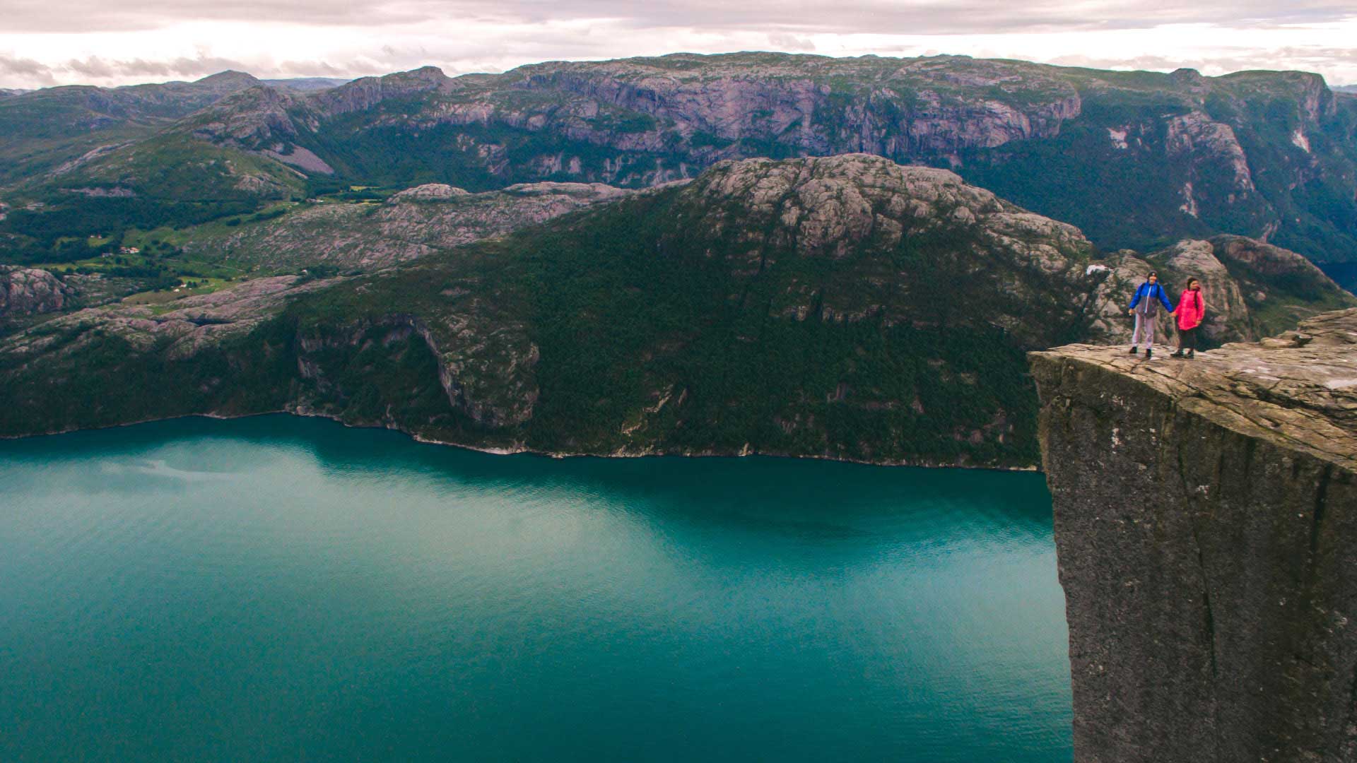 couple standing atop pulpit rock with backdrop of mountains